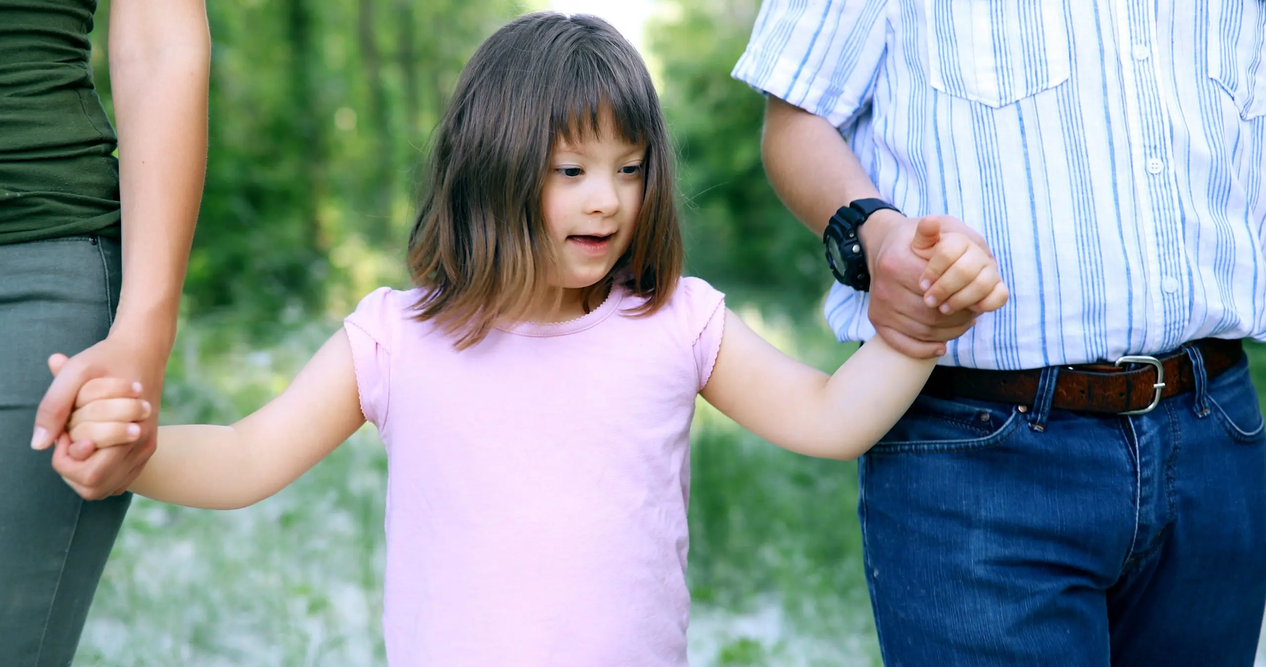 Young child with SEND walking holding hands with two adults.