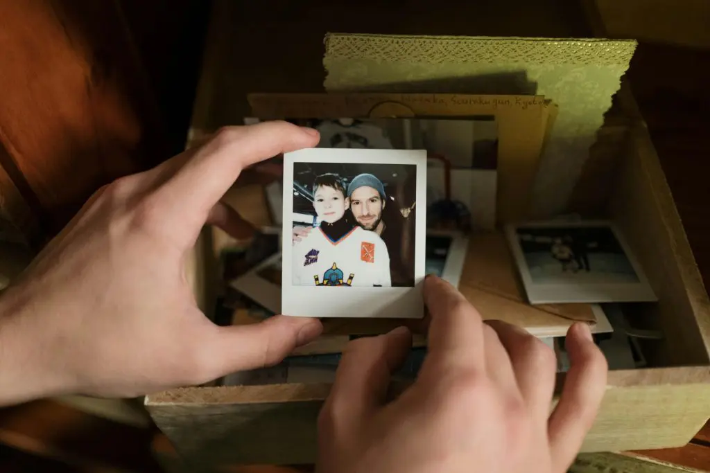 Hands holding a polaroid photo of a child with their dad