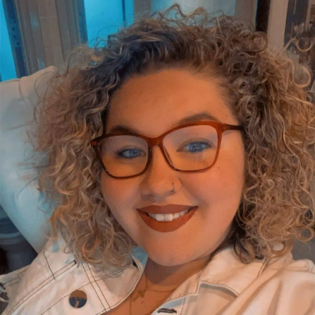 Grace, a young woman with curly hair and glasses, smiling. Grace is a Youth Advisory Trustee at Winston's Wish