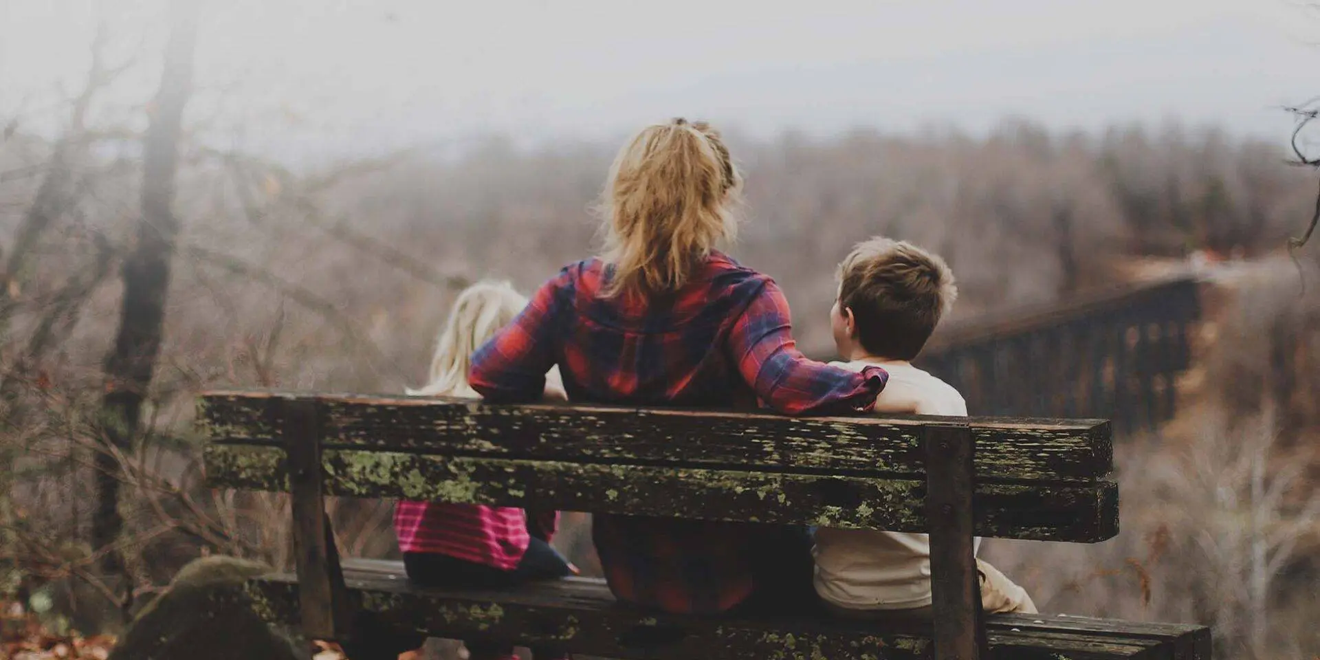 Mum and two young children sat on a bench looking at countryside - bereavement support services from Winston's Wish