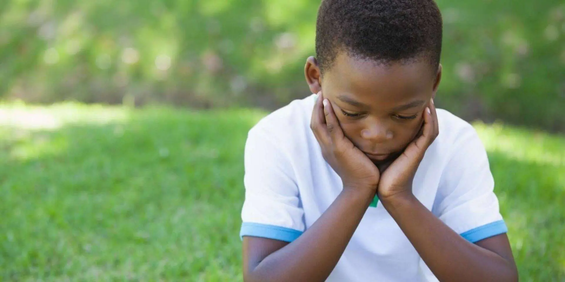Young boy sitting on grass with his head resting in his hands