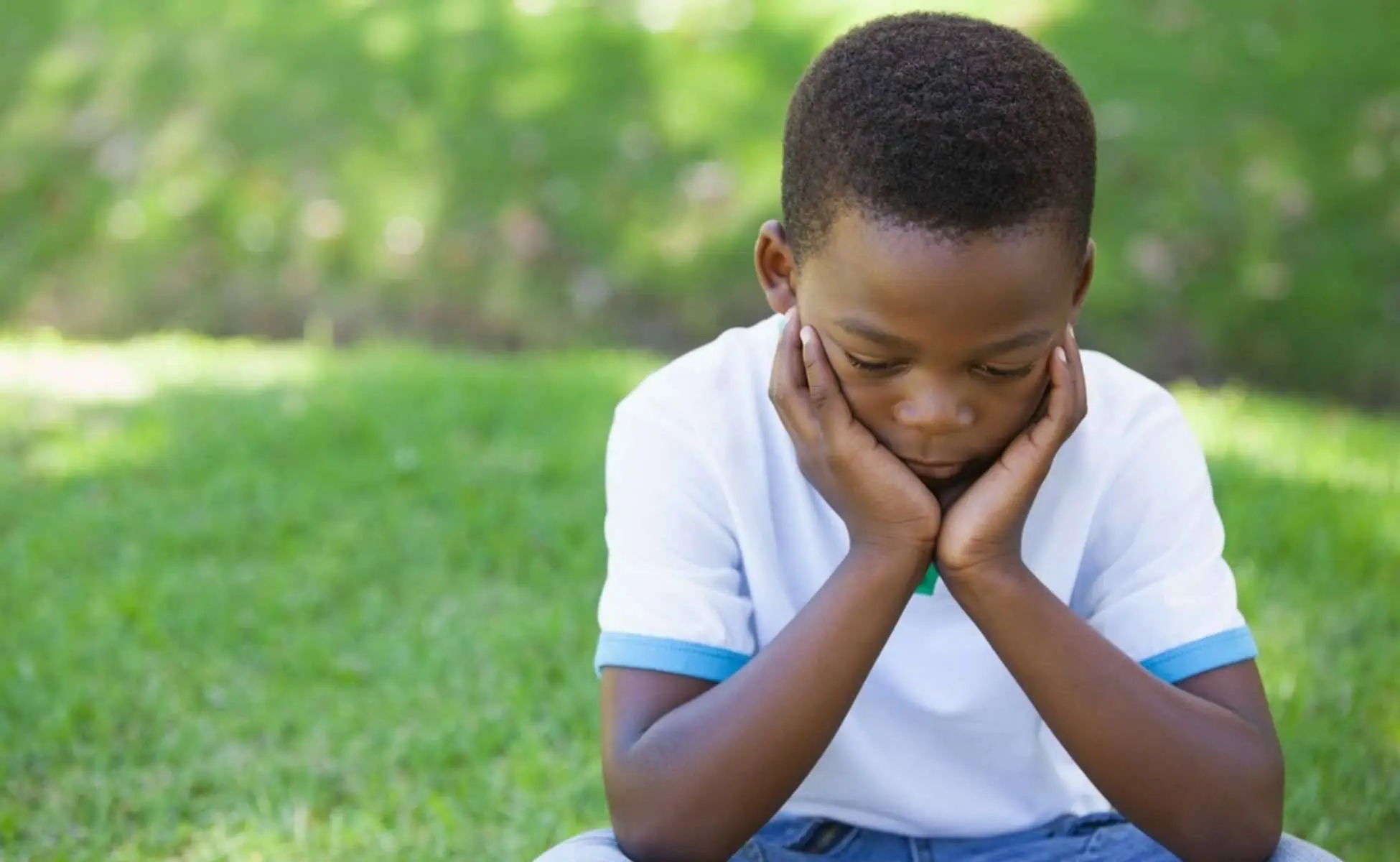 Supporting a child or young person after the death of a parent: Young boy sitting on grass with his head resting in his hands