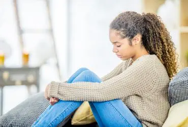 Feelings and thoughts following the death by suicide Young adult sat on sofa holding her knees