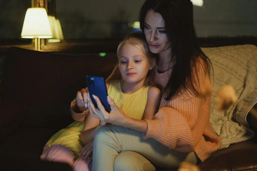 White mum using smartphone with daughter at home.