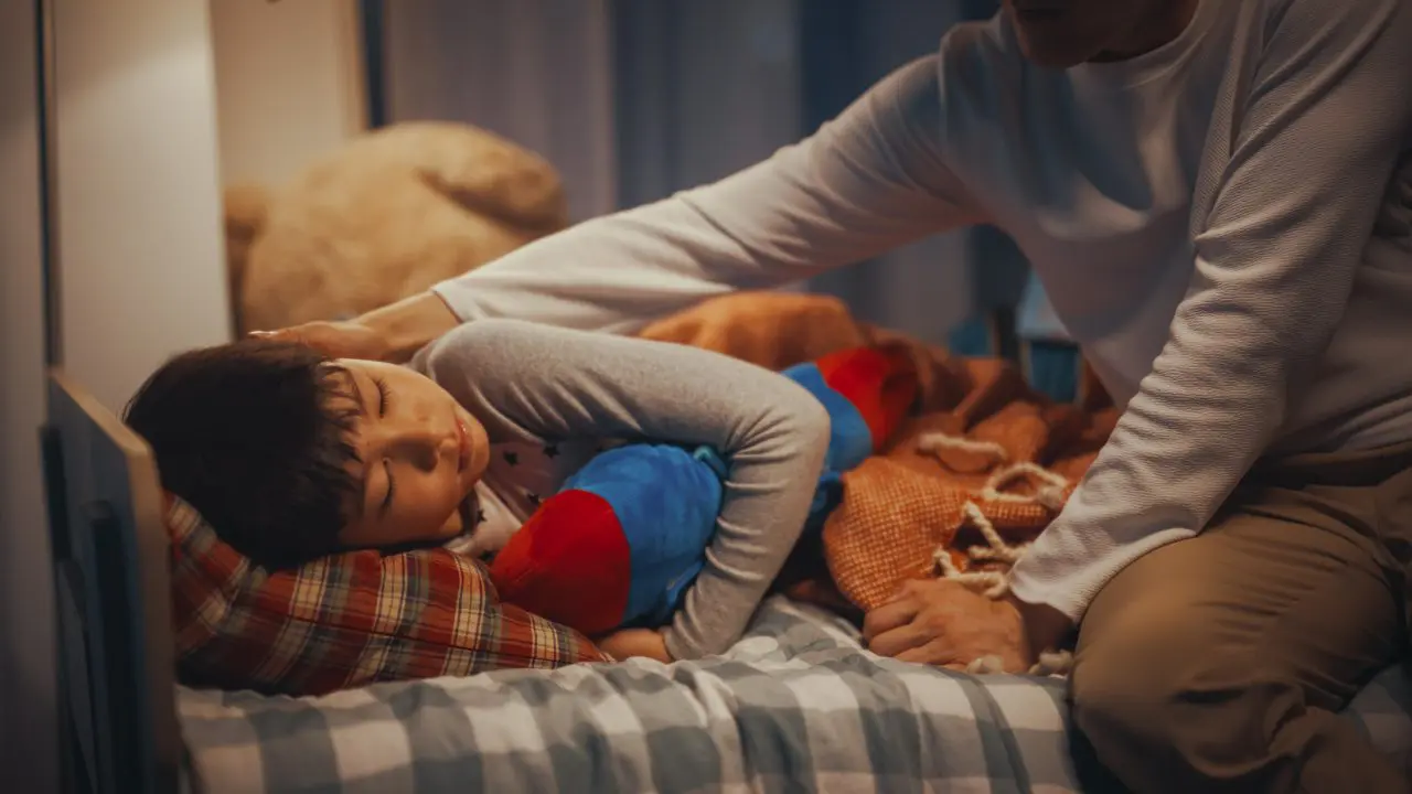 Young boy cuddling toy at bedtime and being comforted by parent