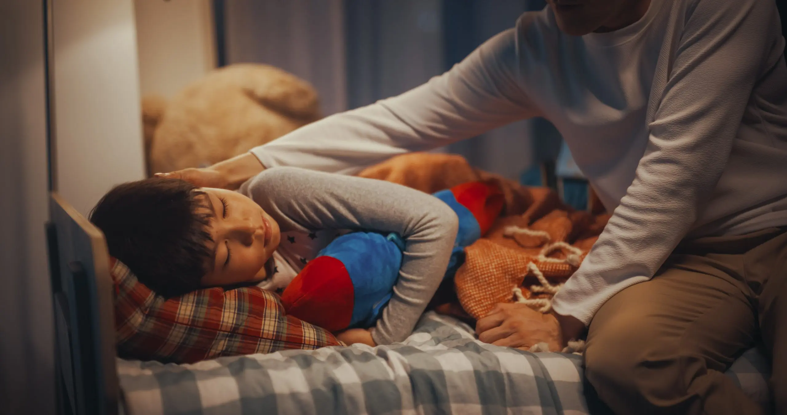 Young boy cuddling toy at bedtime and being comforted by parent