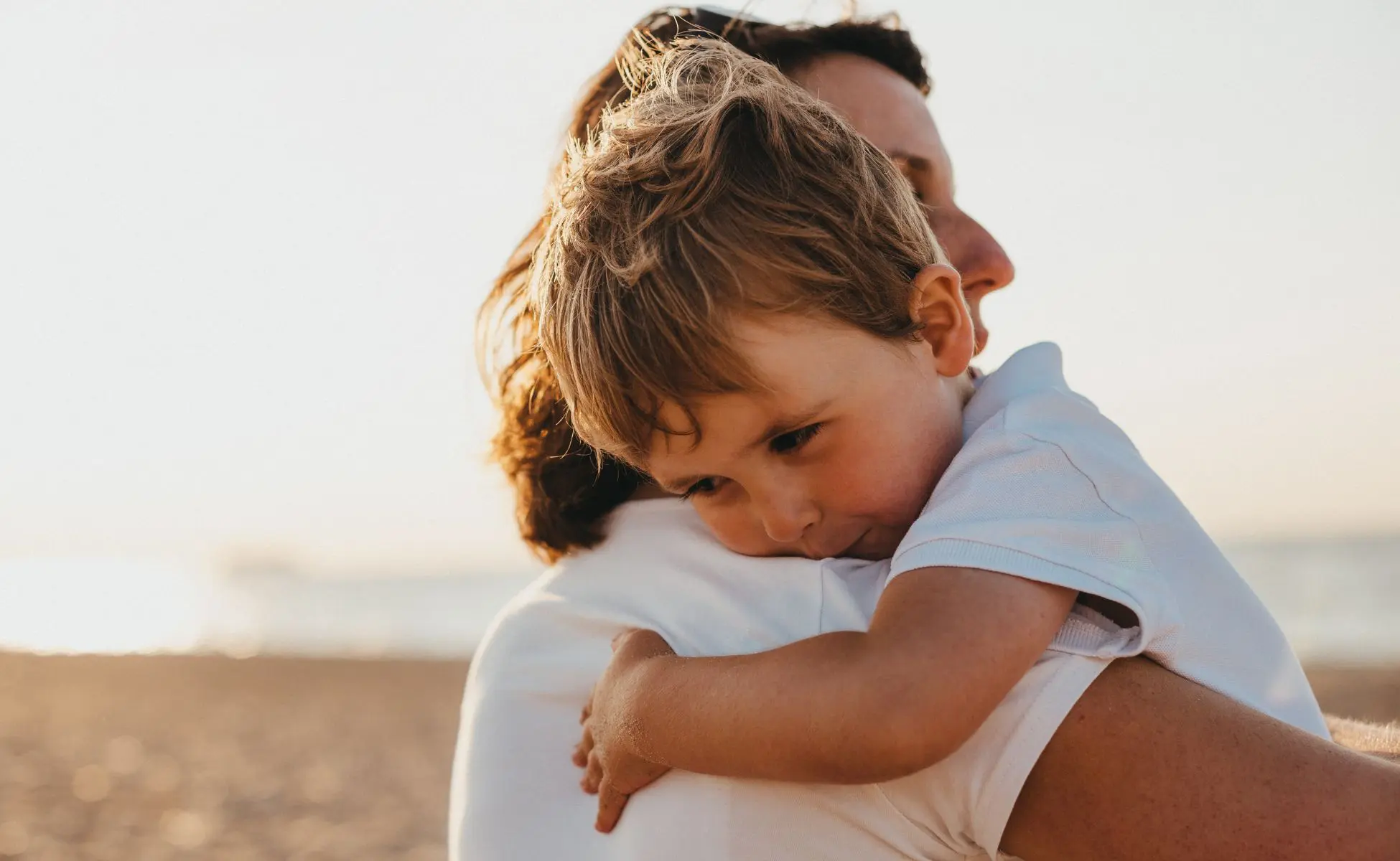 Explaining homicide to children and young people: small blonde boy hugging a parent on a beach front