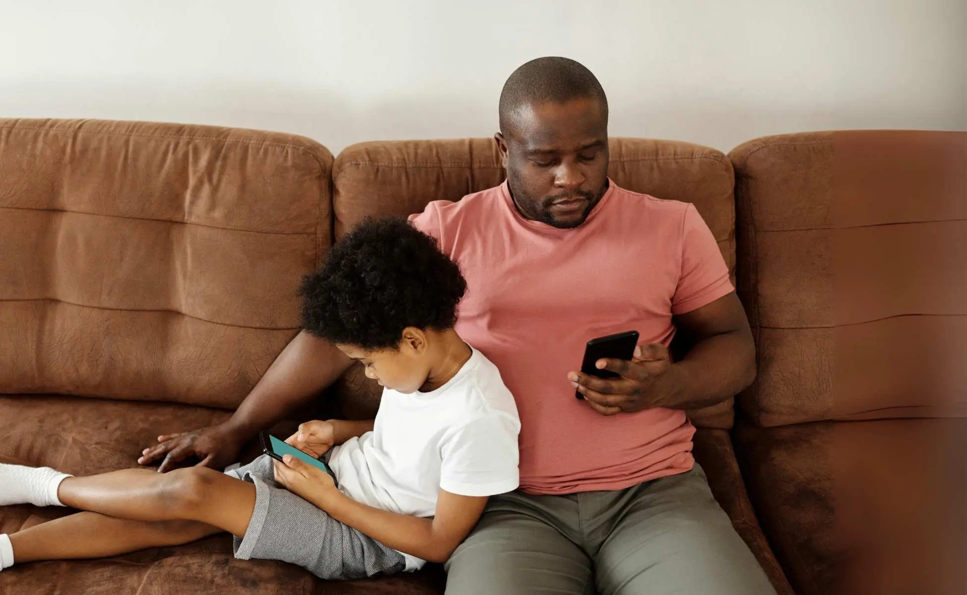 Dad and son sat on sofa both looking at phones