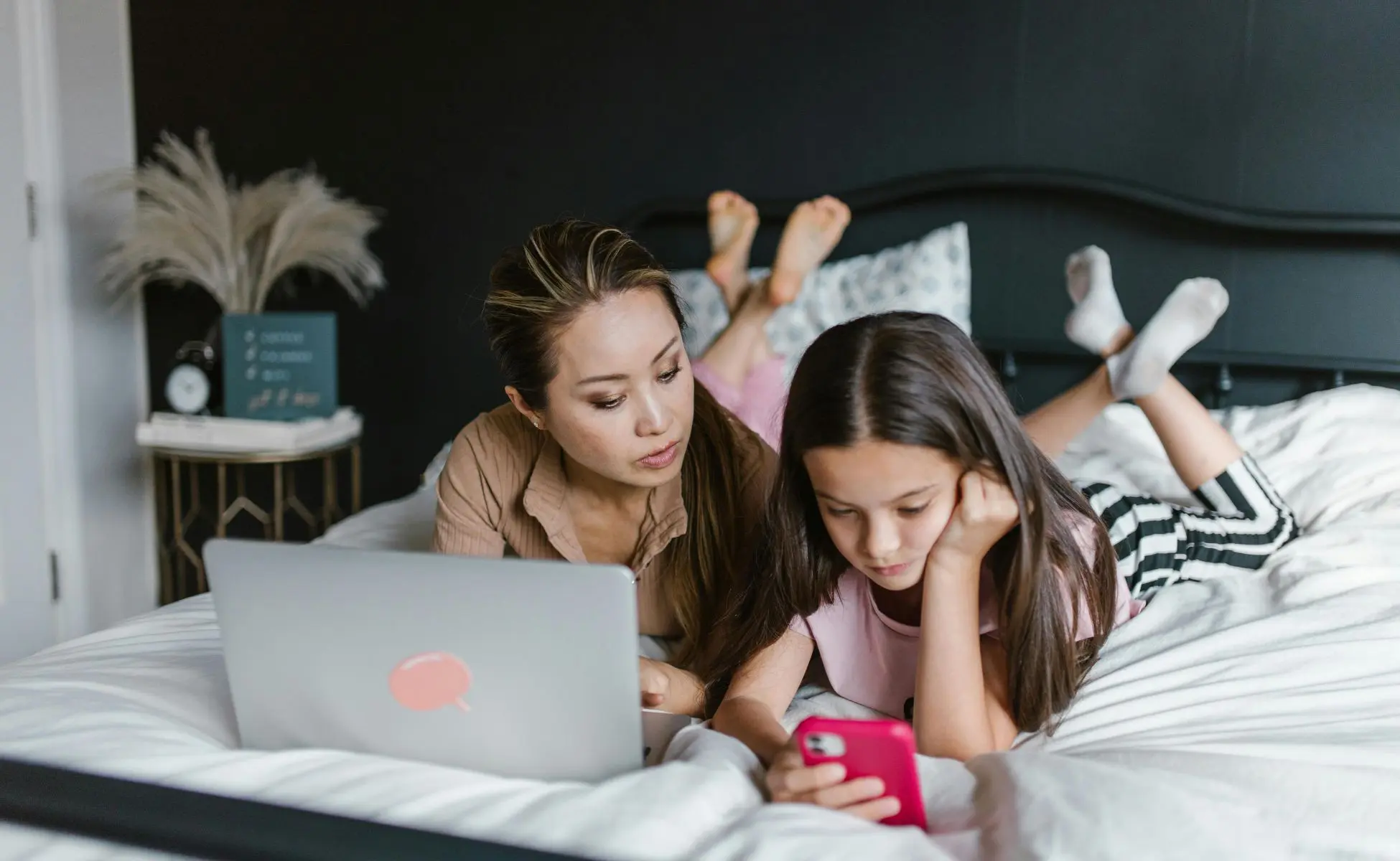 Supporting a grieving teenager: mum and daughter lying on bed while the daughter plays on her phone
