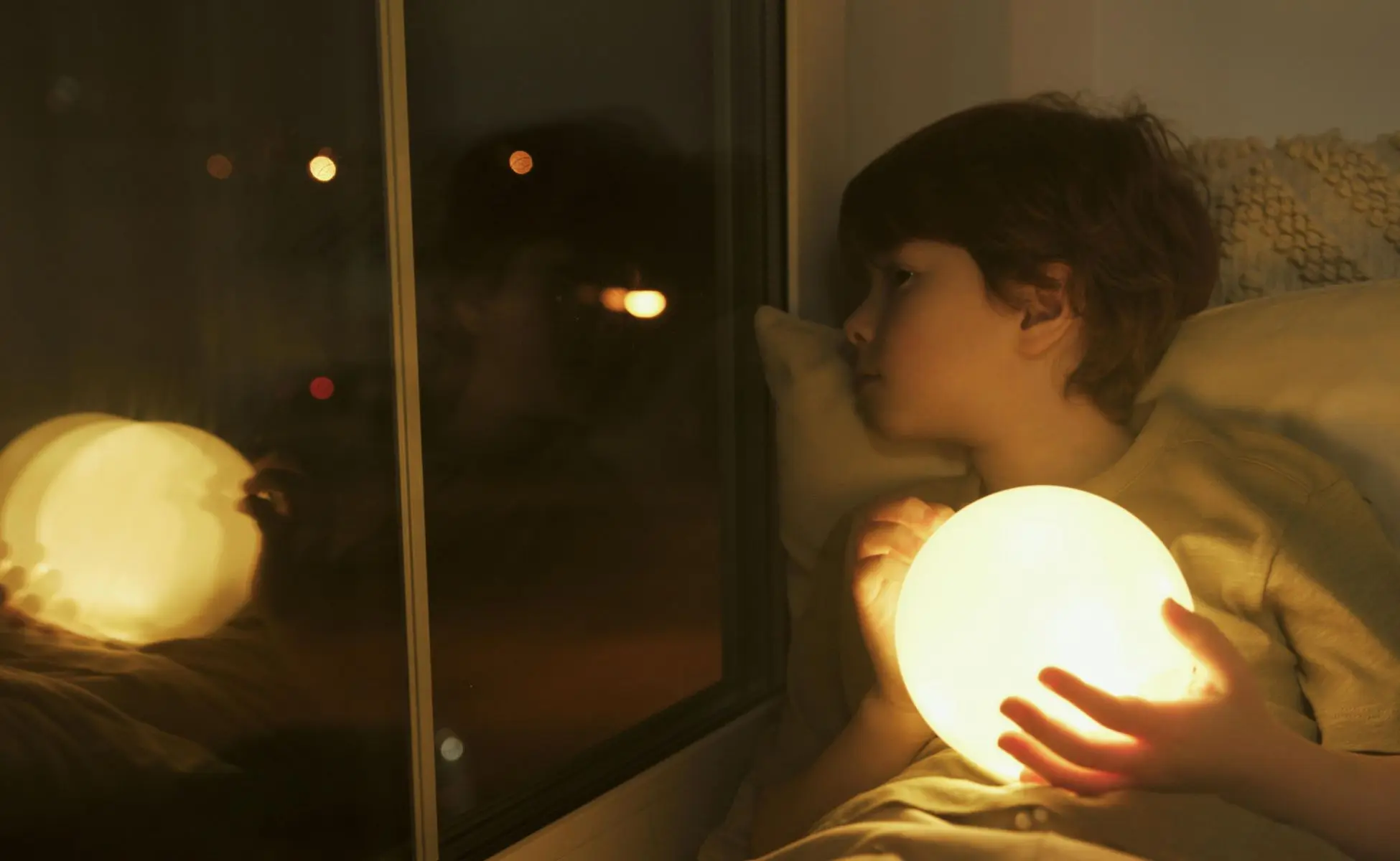 Supporting bereaved children with no memories of their person: small boy holding a night light and looking out of a dark window