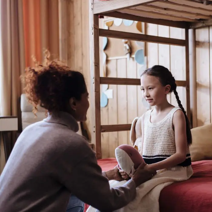 Supporting bereaved children with no memories of their person: Woman talking with her daughter who is sat on a bunk bed holding a soft toy