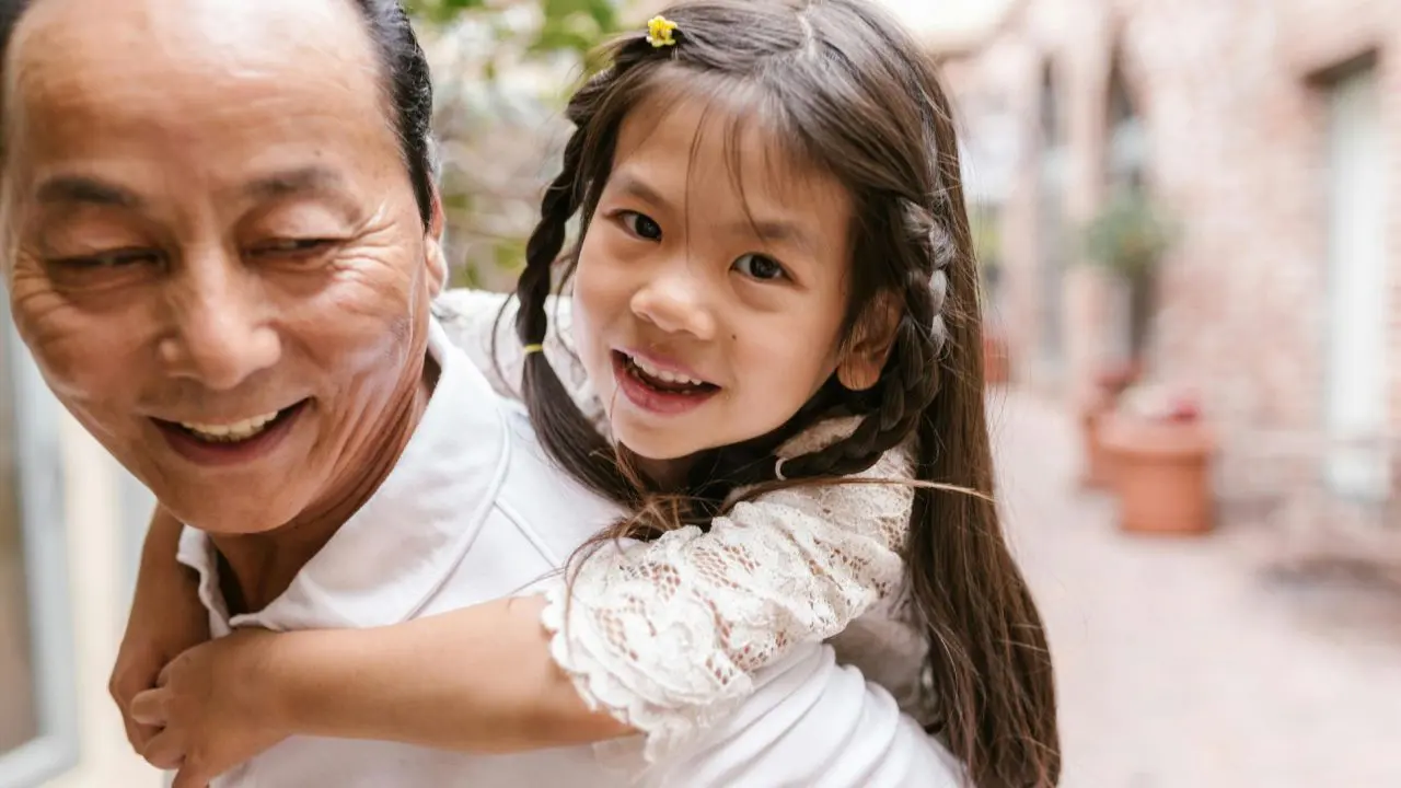 Activities for bereaved children with no memories: Image featuring an older Asian man giving a piggy back ride to a small girl with platted hair