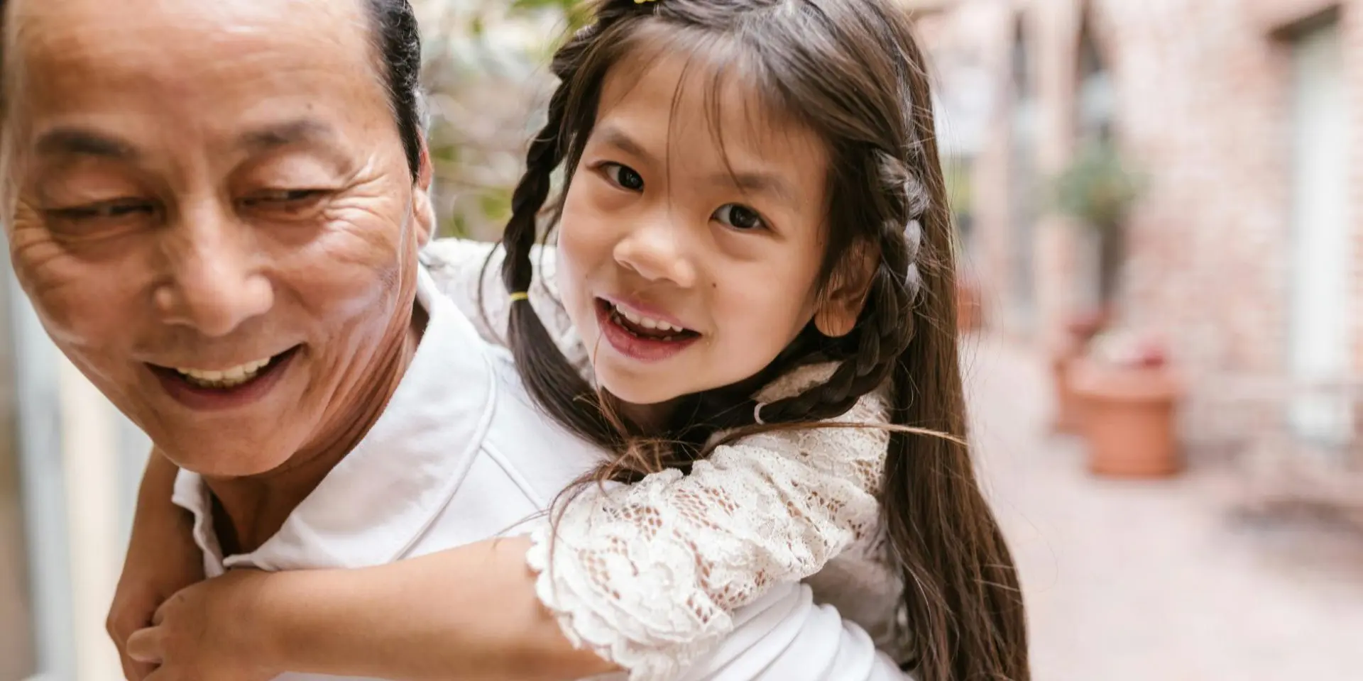 Activities for bereaved children with no memories: Image featuring an older Asian man giving a piggy back ride to a small girl with platted hair