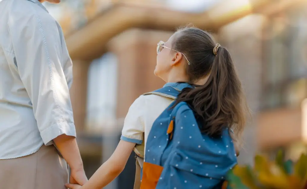 School child with backpack holding mum's hand