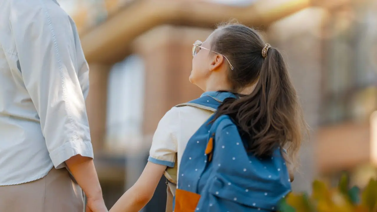 School child with backpack holding mum's hand