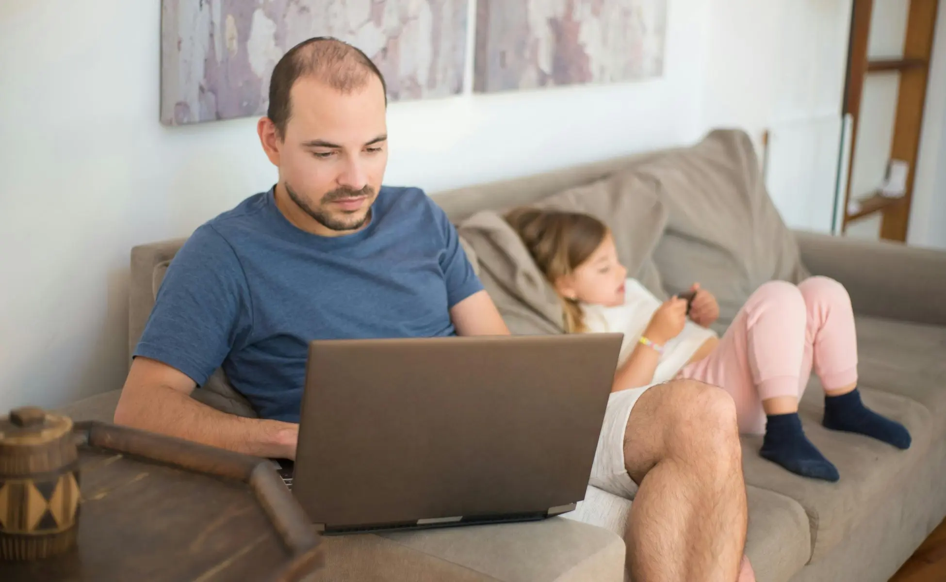 Supporting a child when their friend at school has died. Image featuring a man on his laptop with his child sat next to him on the sofa