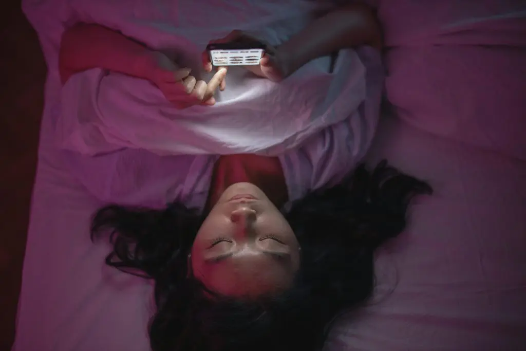 Teenager lying in bed scrolling on their phone at night.