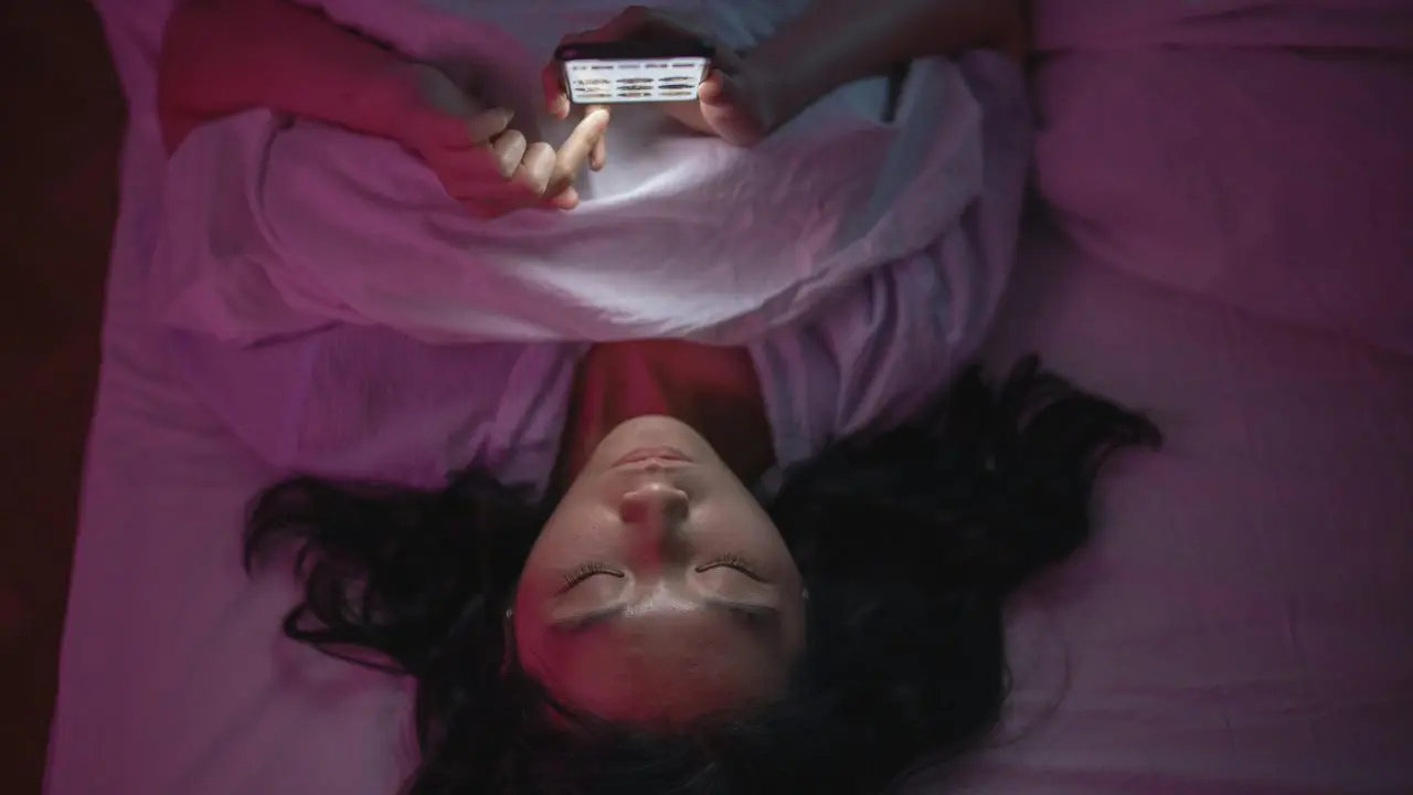 Teenager lying in bed scrolling on their phone at night.