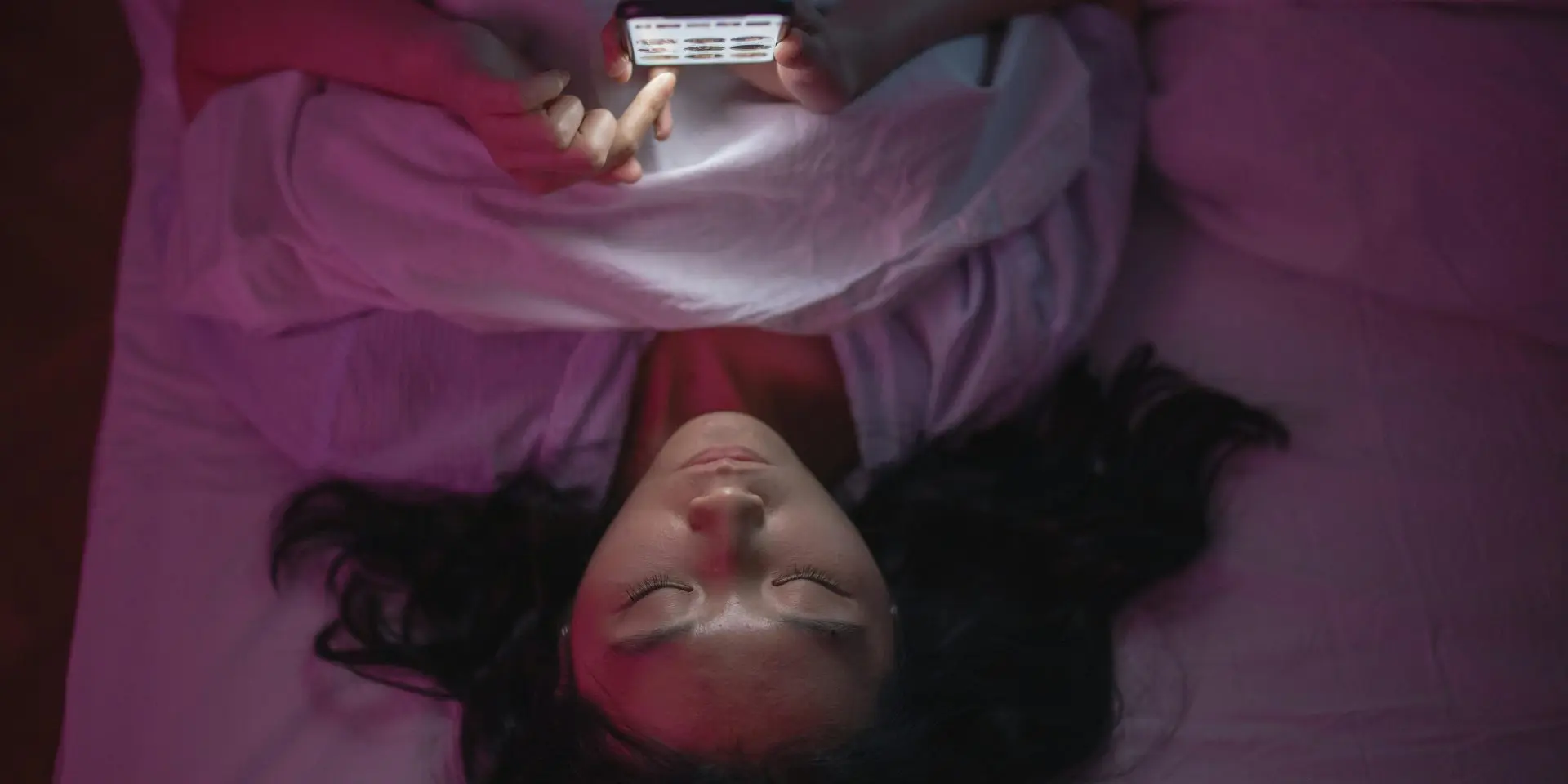 Teenager lying in bed scrolling on their phone at night.