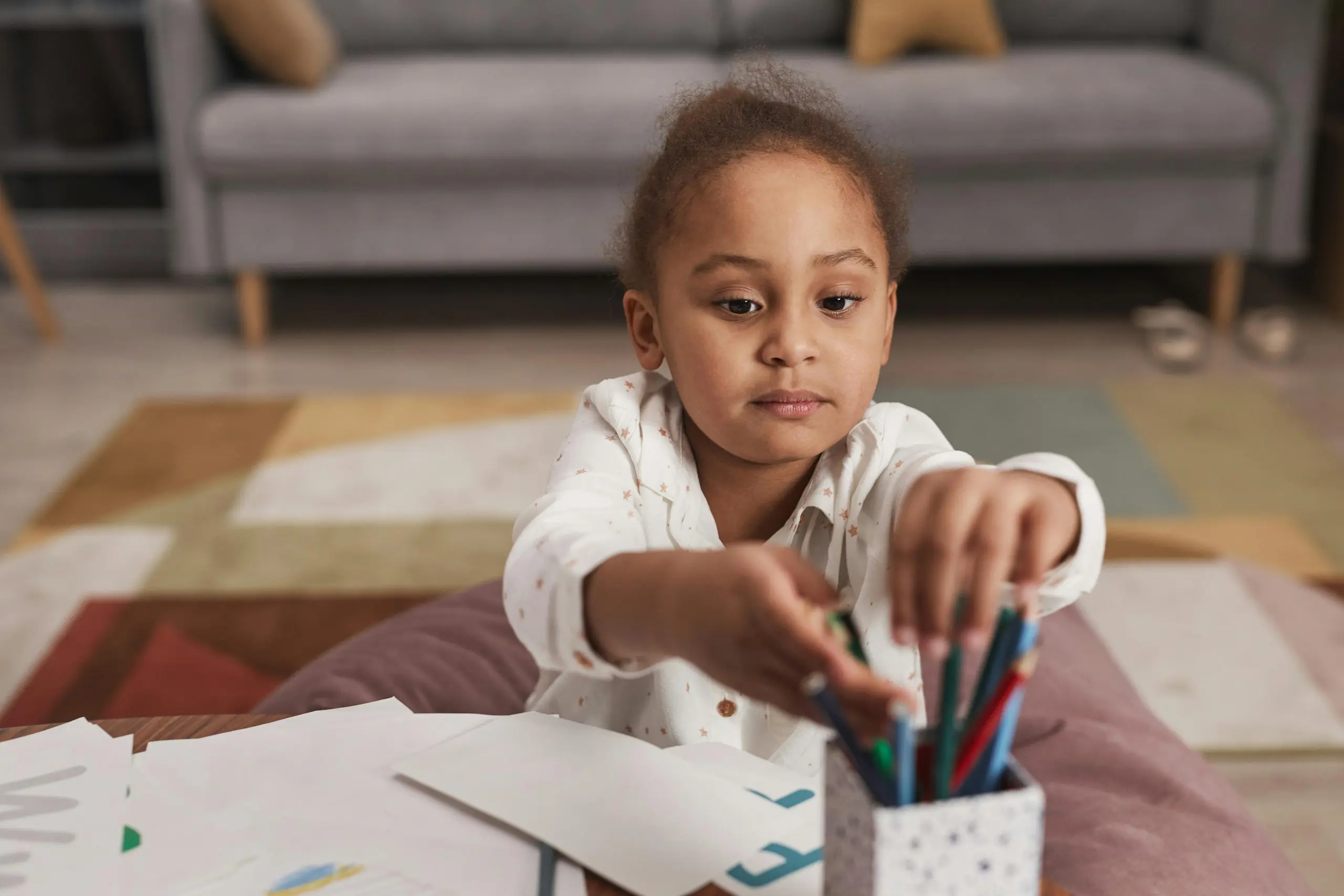 Young child reaching for a coloured pencil with paper in front of them for drawing
