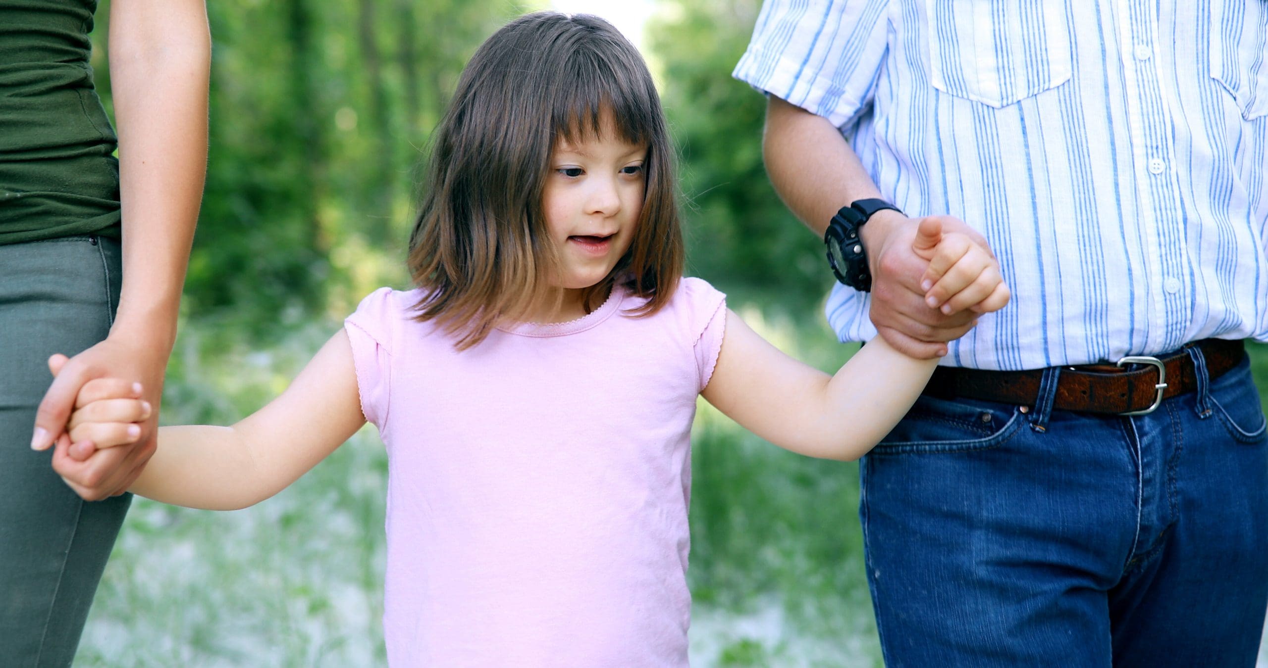 Young child with SEND walking holding hands with two adults.