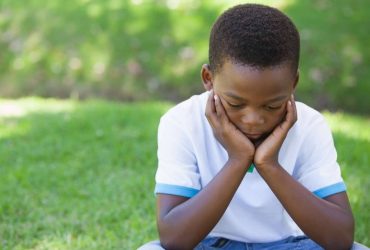 Supporting a child or young person after the death of a parent: Young boy sitting on grass with his head resting in his hands