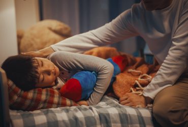 Young boy cuddling toy at bedtime and being comforted by parent