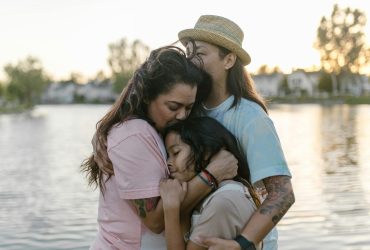 Supporting a child with their grief and mental health. Image featuring a mother hugging her teenager and young child in front of a lake