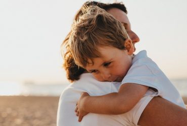 Explaining homicide to children and young people: small blonde boy hugging a parent on a beach front
