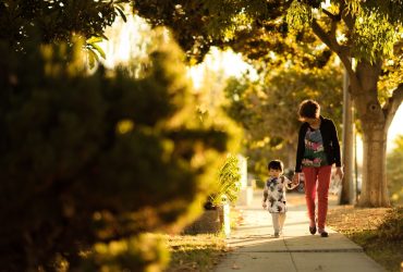 How to prepare children for the death of someone important: image with a Asian woman holding the hand of a small child as they walk down a path shielded by trees