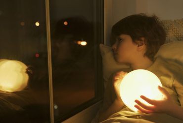 Supporting bereaved children with no memories of their person: small boy holding a night light and looking out of a dark window