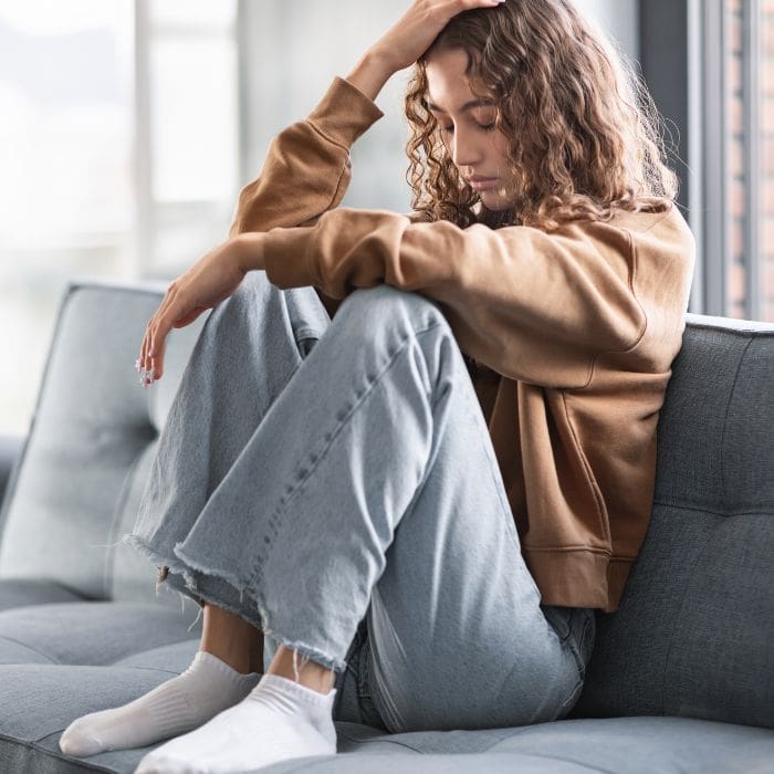What not to say to grieving young people. Teenage girl sat on the sofa looking sad and frustrated