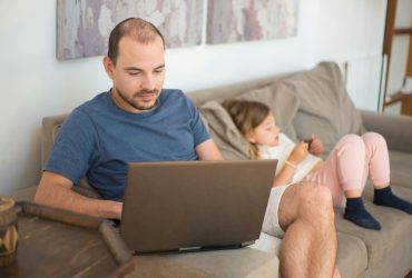 Supporting a child when their friend at school has died. Image featuring a man on his laptop with his child sat next to him on the sofa