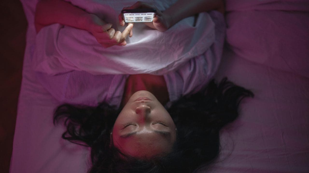 Teenager lying in bed scrolling on their phone at night.